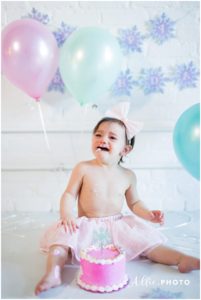 one year old girl does cake smash with pink cake for birthday portraits